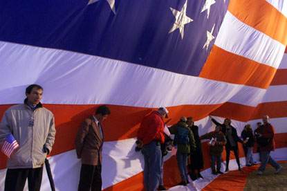 On a very windy day, a group attempts to secure the American flag as they wait for President Clinton to give a speech.